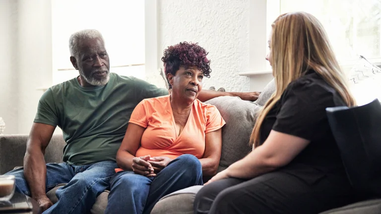 Image shows three people sat on sofa talking