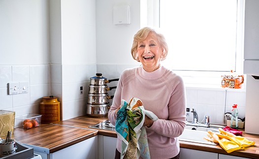 Woman in kitchen laughing while drying dishes