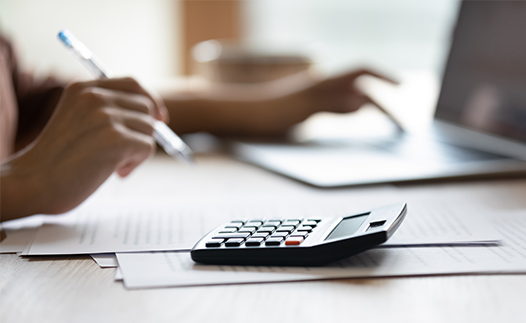 Person using laptop, calculator and holding a pen