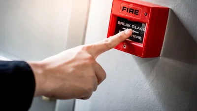 Image shows a person pressing a red fire alarm