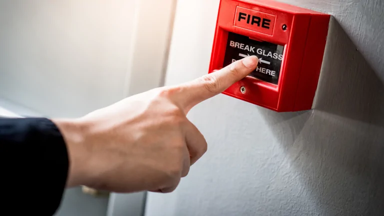 Image shows a person pressing a red fire alarm
