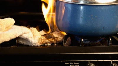 Image shows a towel and saucepan on fire on a gas stove