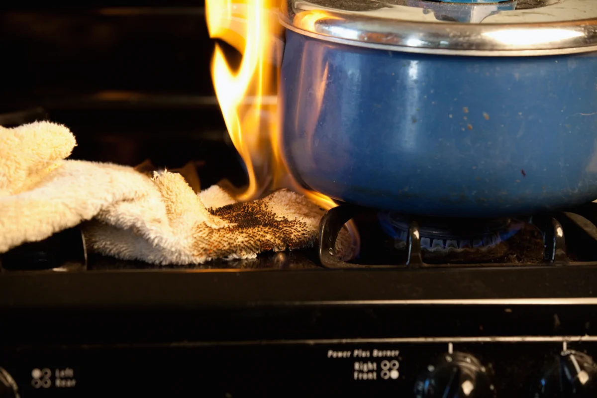 Image shows a towel and saucepan on fire on a gas stove
